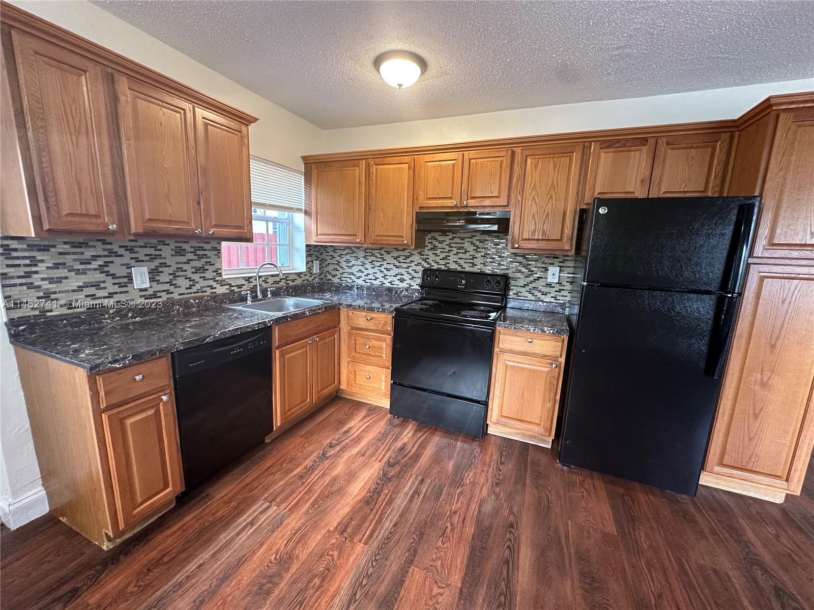 a kitchen with stainless steel appliances granite countertop a refrigerator a sink dishwasher a stove top oven a refrigerator and dishwasher with wooden floor