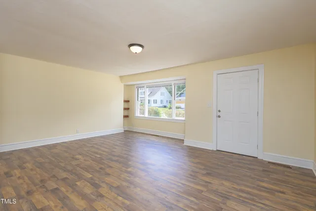 a view of an empty room with window and wooden floor