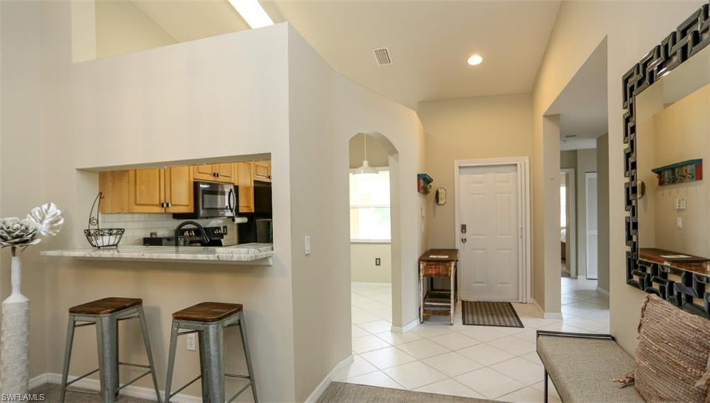 6645 Huntington Lakes Circle, Unit 201 Naples, FL 34119 - Photo 11 of 48 Kitchen featuring a breakfast bar, decorative backsplash, light tile patterned floors, and kitchen peninsula