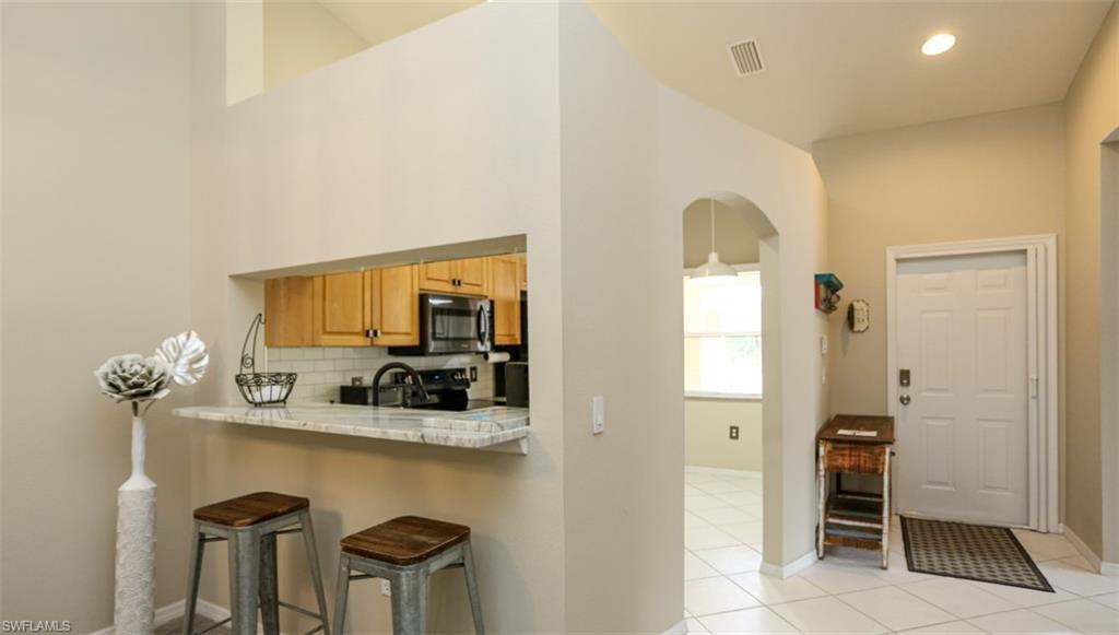6645 Huntington Lakes Circle, Unit 201 Naples, FL 34119 - Photo 12 of 48 Kitchen featuring backsplash, a kitchen breakfast bar, appliances with stainless steel finishes, light tile patterned flooring, and light stone counters