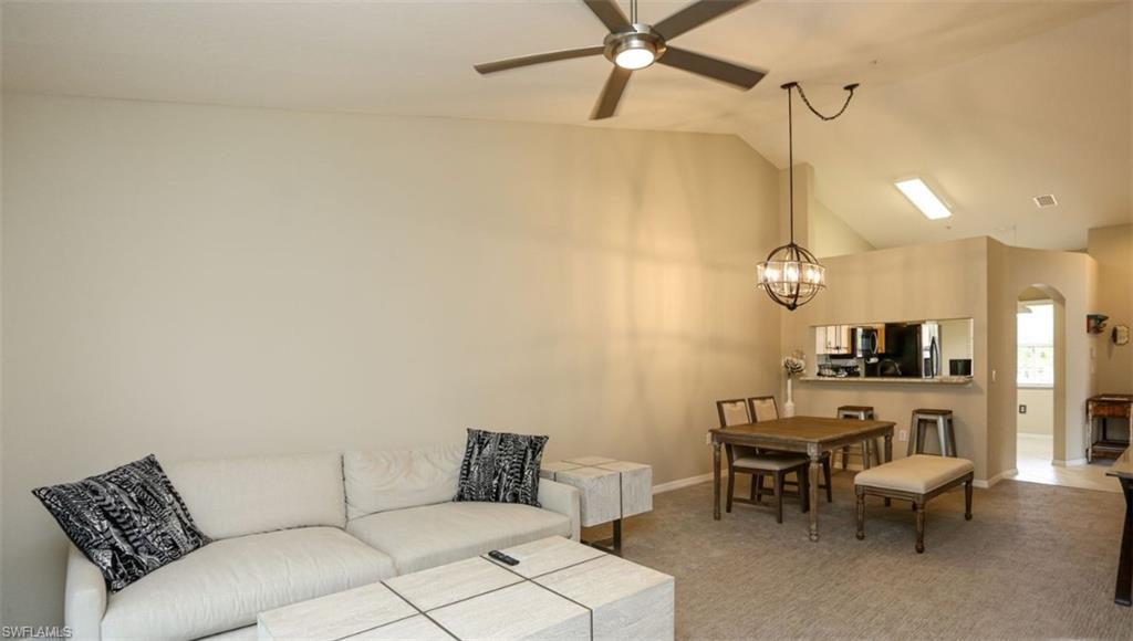 6645 Huntington Lakes Circle, Unit 201 Naples, FL 34119 - Photo 2 of 48 Carpeted living room with ceiling fan with notable chandelier and vaulted ceiling