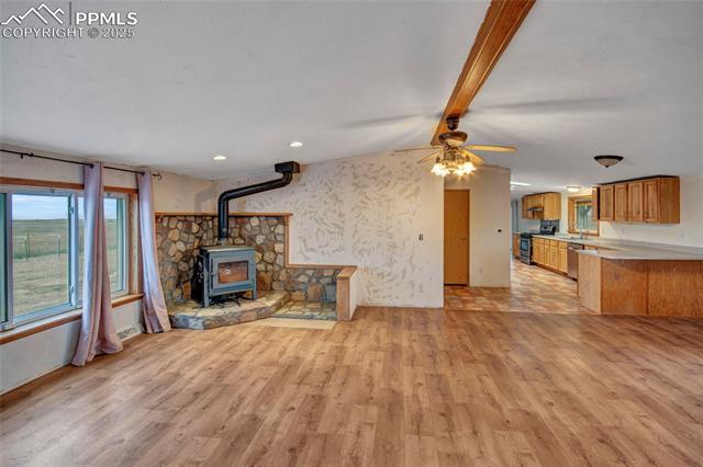 7940 Edison Road Yoder, CO 80864 - Photo 12 of 38 Unfurnished living room with a wood stove, beamed ceiling, light wood-type flooring, a ceiling fan, and wallpapered walls