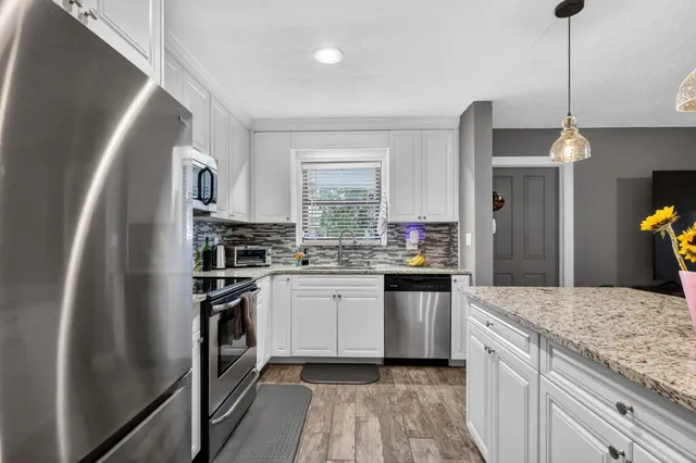 a kitchen with stainless steel appliances granite countertop a refrigerator a sink dishwasher a stove and white cabinets with wooden floor