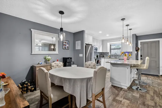 a dining room with stainless steel appliances kitchen island granite countertop a dining table chairs and a refrigerator