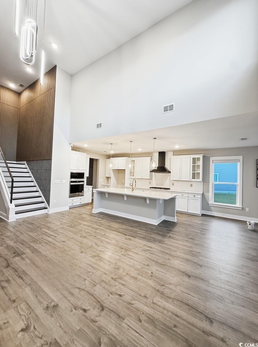 2108 Ballast Court Myrtle Beach, SC 29579 - Photo 7 of 37 Kitchen with a towering ceiling, pendant lighting, tasteful backsplash, white cabinetry, and wall chimney exhaust hood