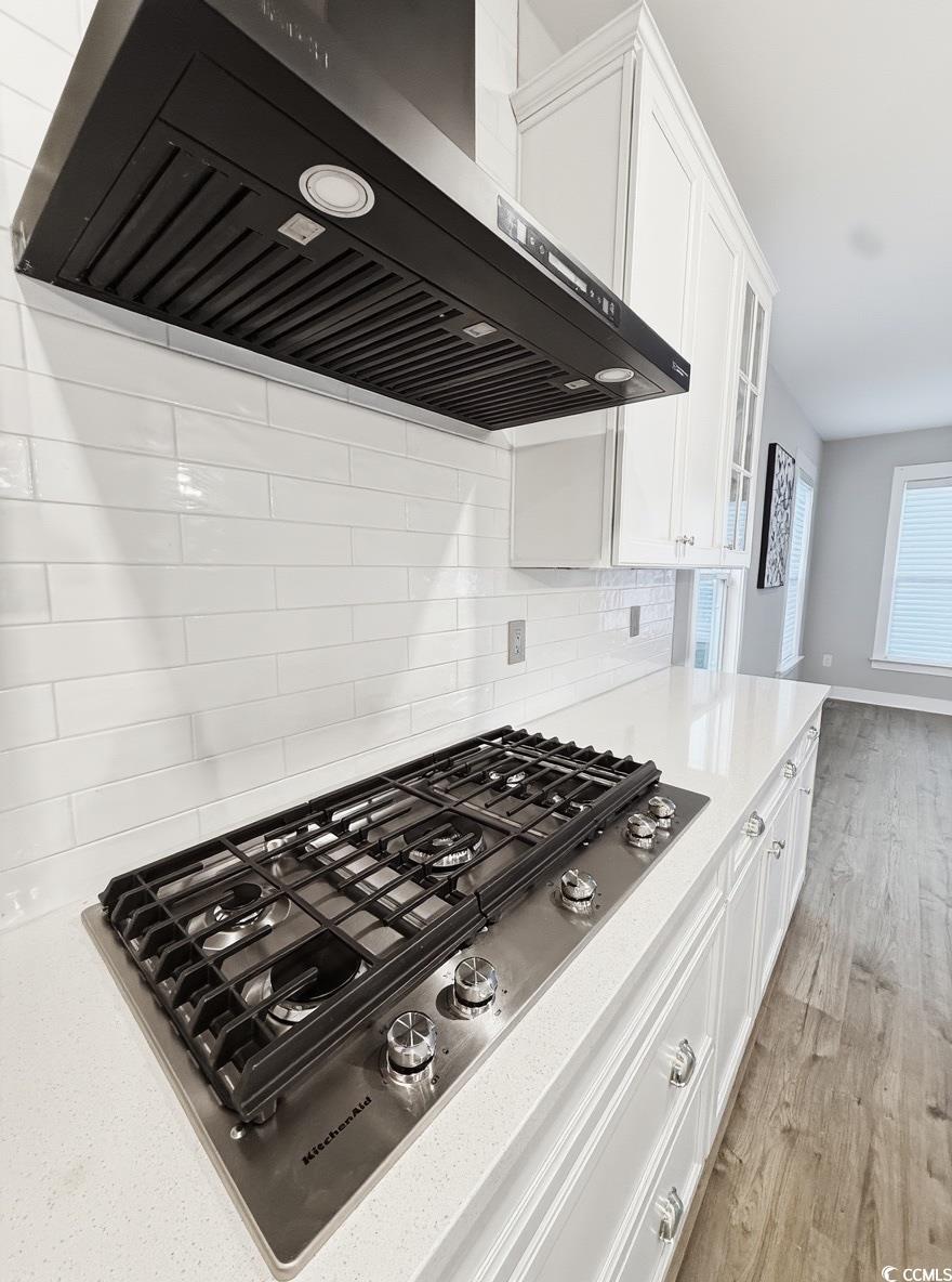 2108 Ballast Court Myrtle Beach, SC 29579 - Photo 9 of 37 Kitchen featuring wall chimney range hood, stainless steel gas cooktop, white cabinets, backsplash, and light stone countertops