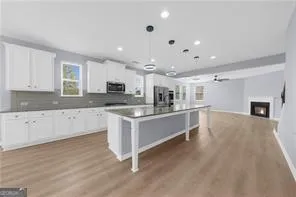 a large kitchen with stainless steel appliances granite countertop a stove a sink a refrigerator and white cabinets with wooden floor