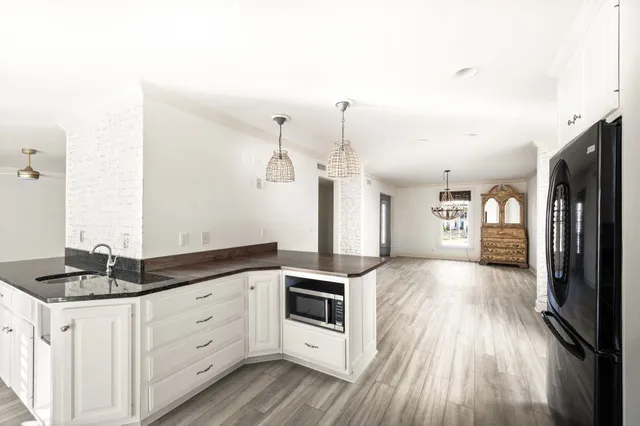 a kitchen with granite countertop a refrigerator a stove a sink and white cabinets with wooden floor