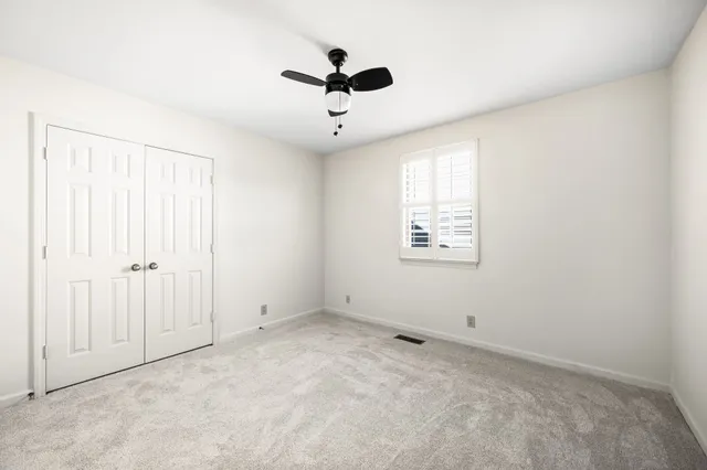 an empty room with ceiling fan and windows