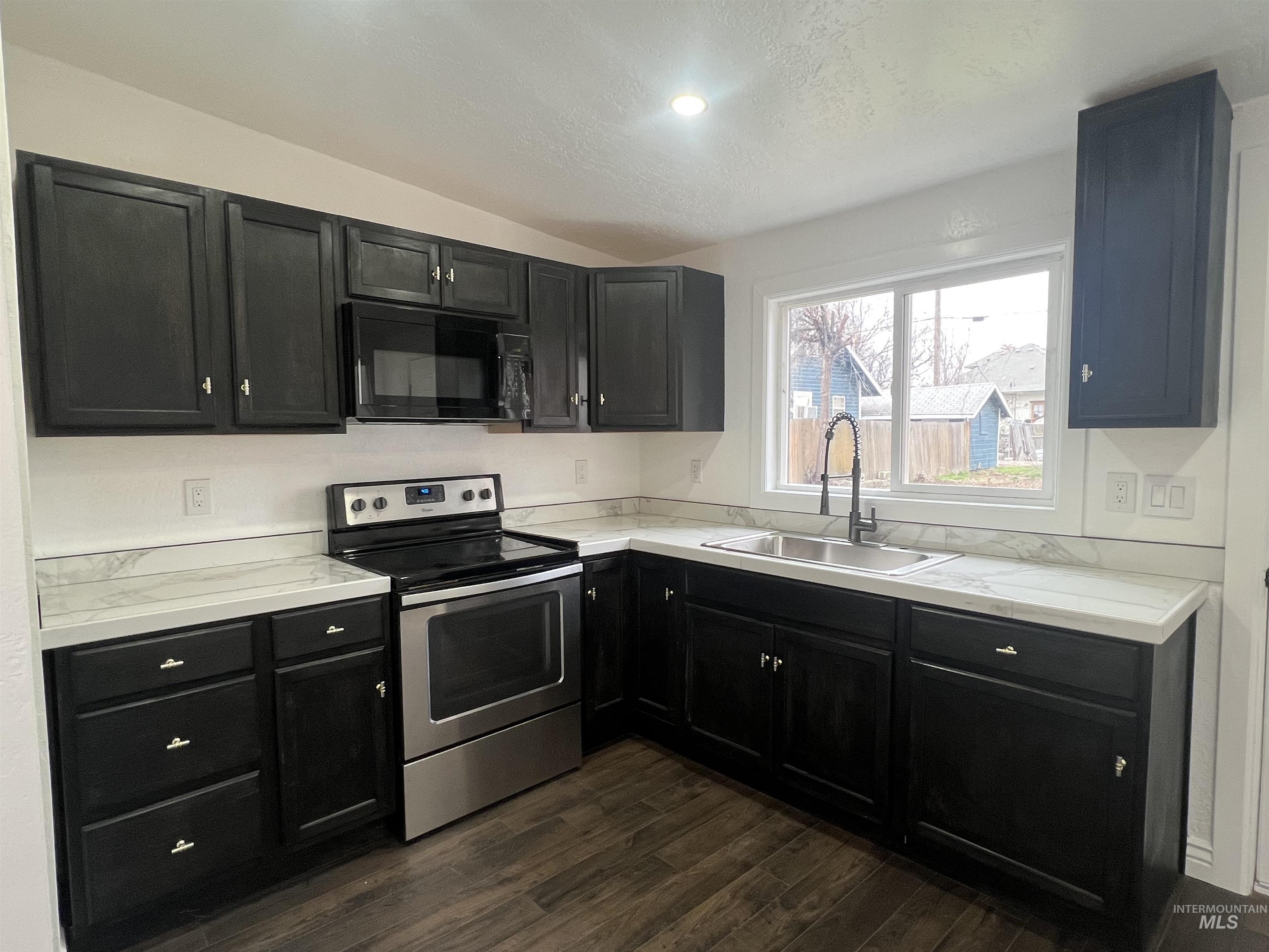 511 North 10th Street Payette, ID 83661 - Photo 4 of 18 Kitchen featuring dark cabinetry, stainless steel range with electric cooktop, light countertops, black microwave, and lofted ceiling