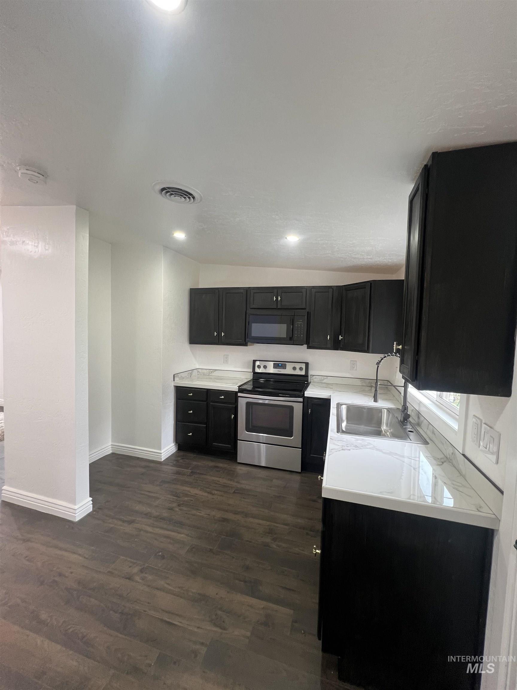 511 North 10th Street Payette, ID 83661 - Photo 5 of 18 Kitchen with dark cabinets, light countertops, stainless steel electric range oven, black microwave, and dark wood-type flooring