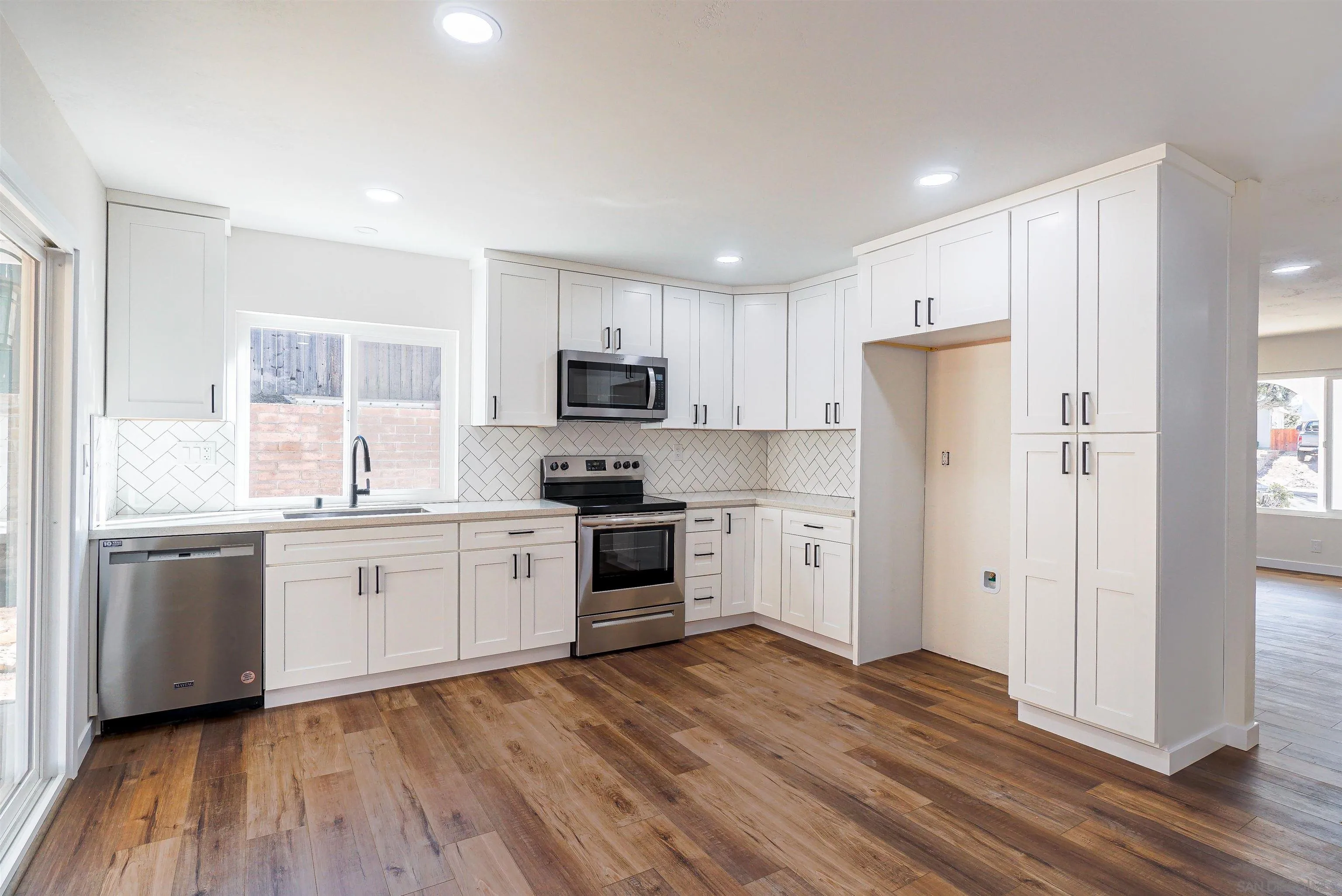 14558 Silla Street Poway, CA 92064 - Photo 6 of 20 a kitchen with a white cabinets a sink a window a wooden floor and stainless steel appliances