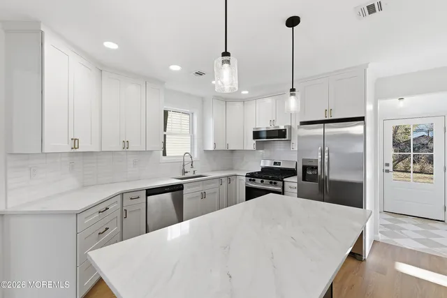 a kitchen with stainless steel appliances kitchen island granite countertop a refrigerator a sink dishwasher a stove and white cabinets with wooden floor