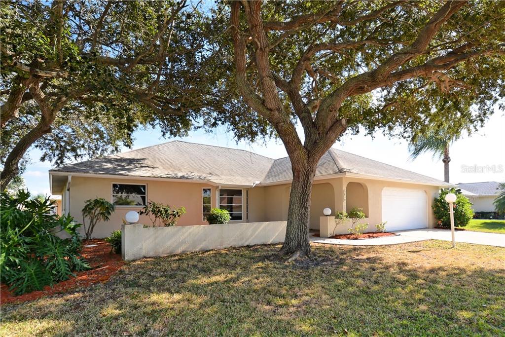 a view of a white house next to a yard with potted plants and large trees