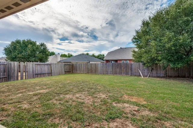 a view of a backyard with large trees and wooden fence