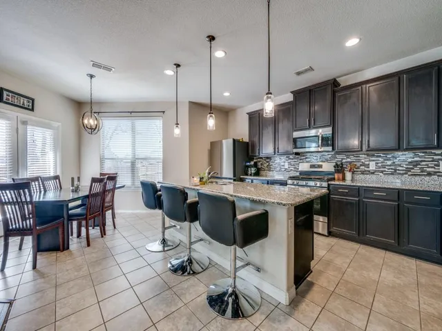 a kitchen with stainless steel appliances granite countertop a stove a sink a refrigerator a dining table and chairs