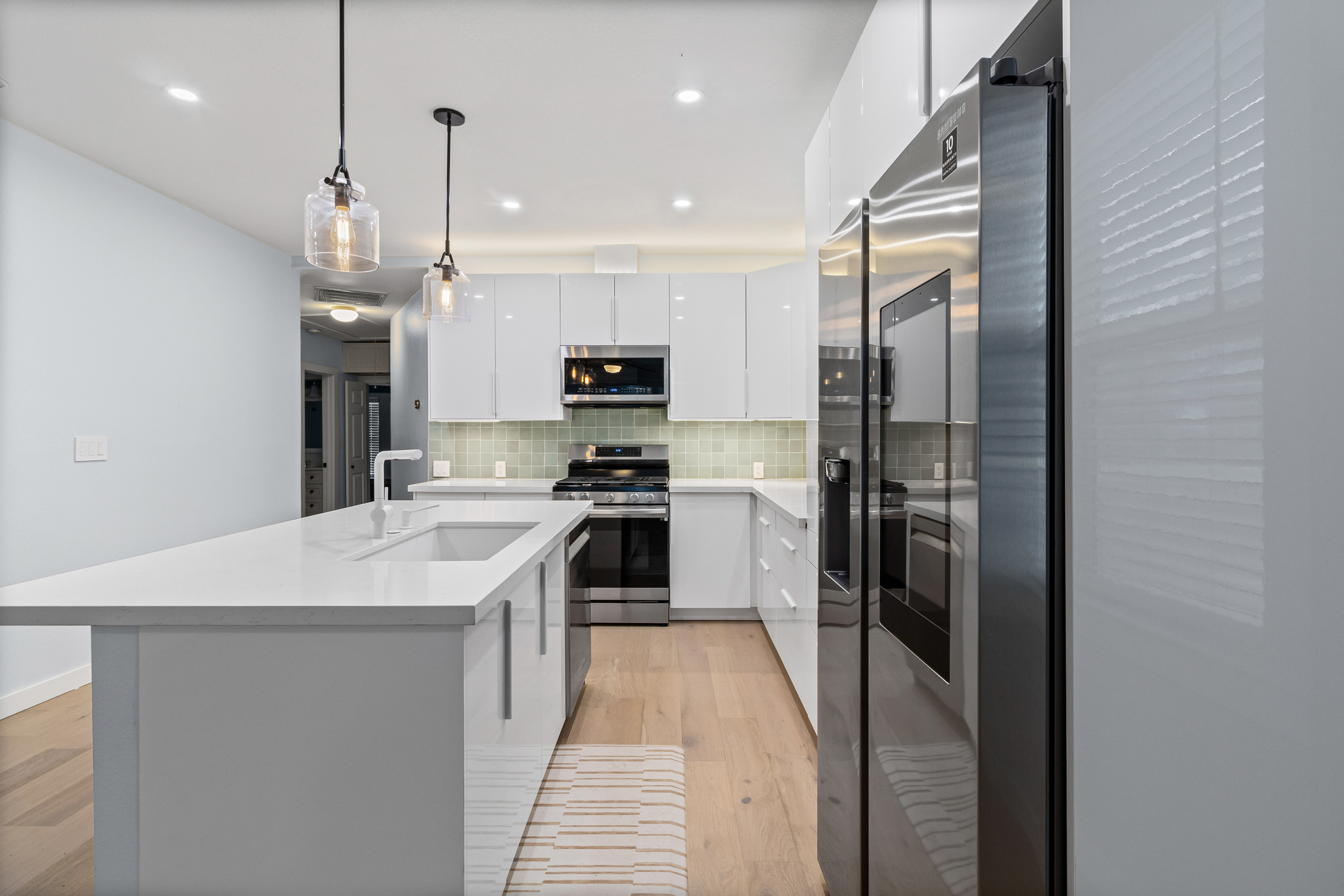 84 Waller Street Austin, TX 78702 - Photo 7 of 22 Kitchen with hanging light fixtures, stainless steel appliances, decorative backsplash, white cabinetry, and modern cabinets