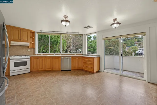 a view of an empty room with a window and kitchen view