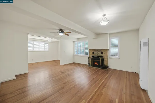 an empty room with wooden floor chandelier fan and windows