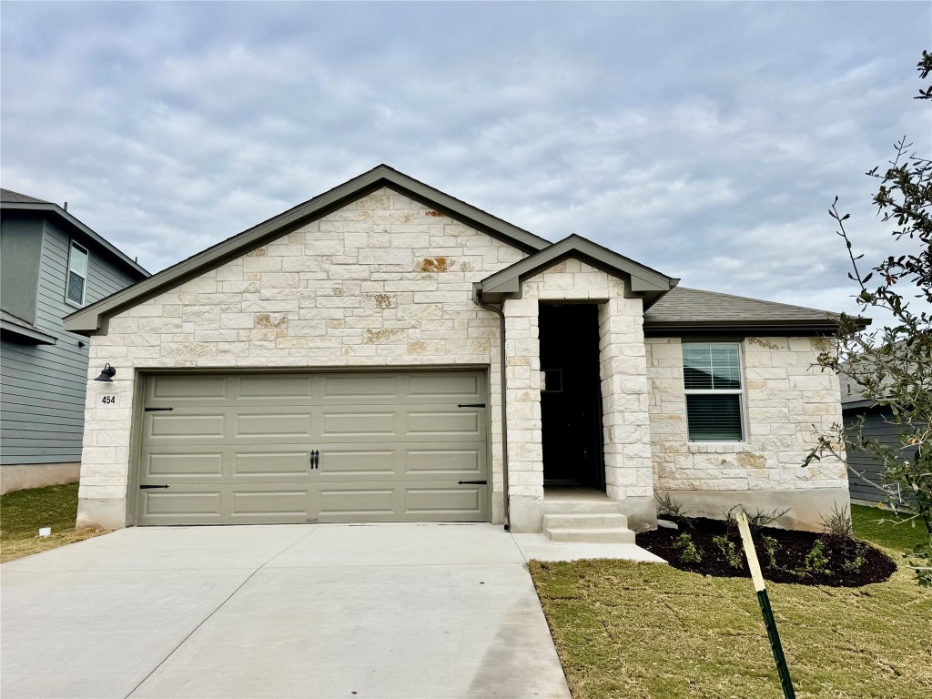 View of front of home with stone siding, concrete driveway, a garage, and a front lawn