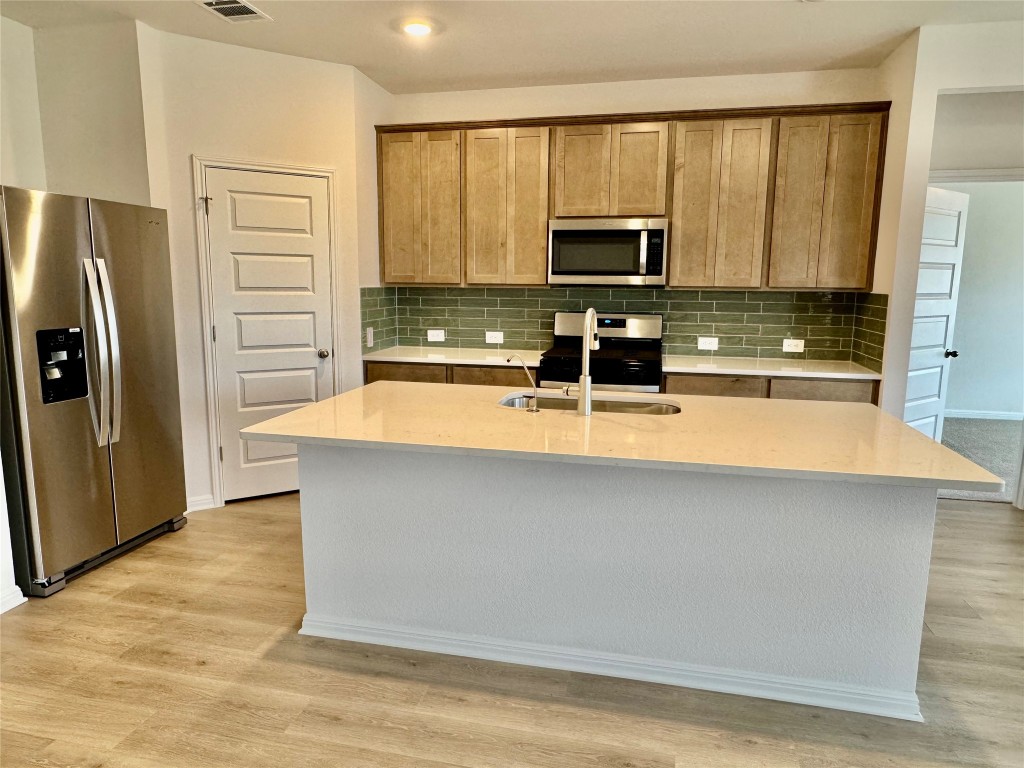 454 El Capitan Loop Dripping Springs, TX 78620 - Photo 2 of 26 Kitchen featuring appliances with stainless steel finishes, light stone countertops, decorative backsplash, and an island with sink