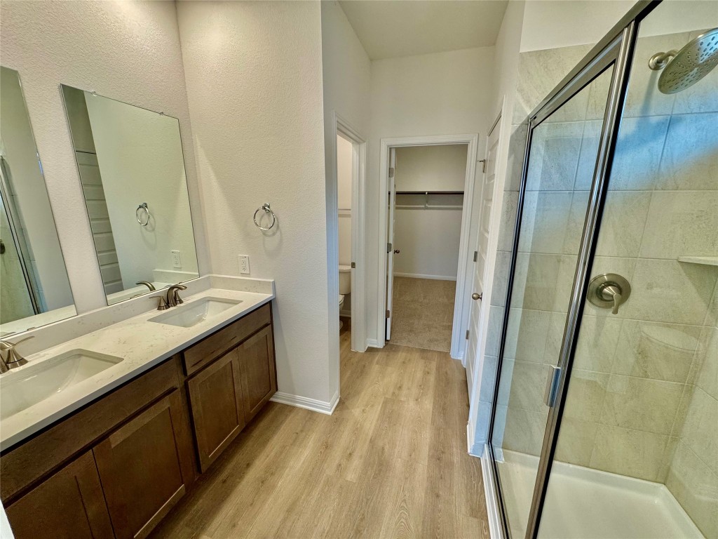 454 El Capitan Loop Dripping Springs, TX 78620 - Photo 4 of 26 Bathroom with a spacious closet, double vanity, a stall shower, and light wood finished floors