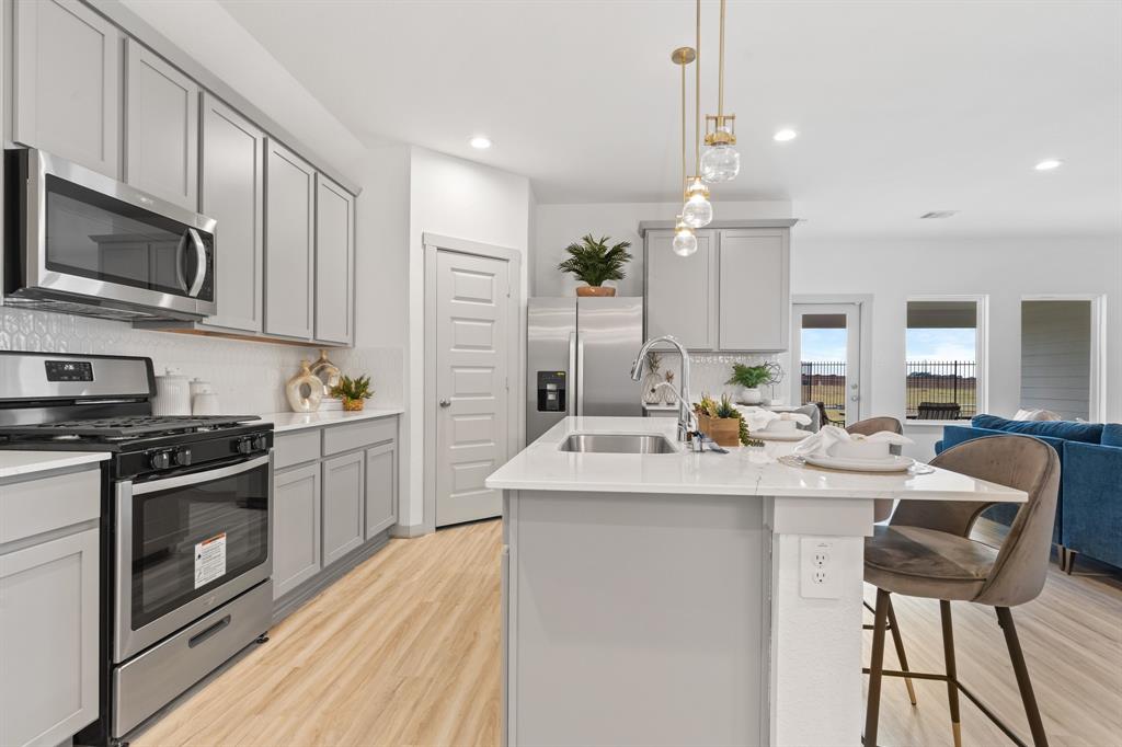 a kitchen with stainless steel appliances kitchen island granite countertop a stove top oven a sink dishwasher and a refrigerator with wooden floor