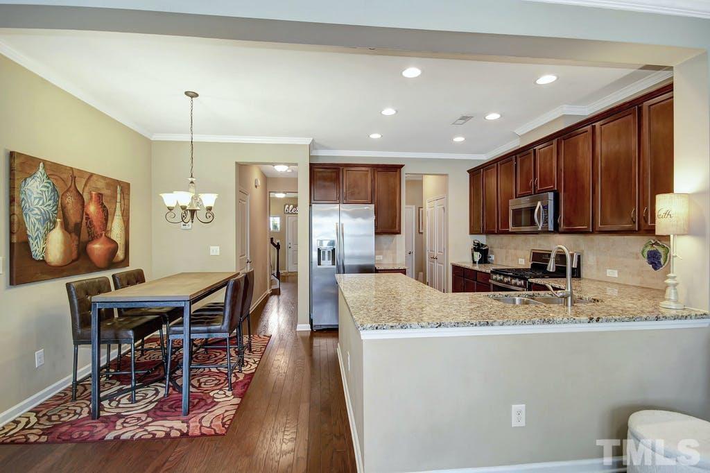 2456 Baslow Drive Apex, NC 27539 - Photo 12 of 39 a kitchen with stainless steel appliances granite countertop a stove top oven a sink dishwasher a dining table and chairs with wooden floor