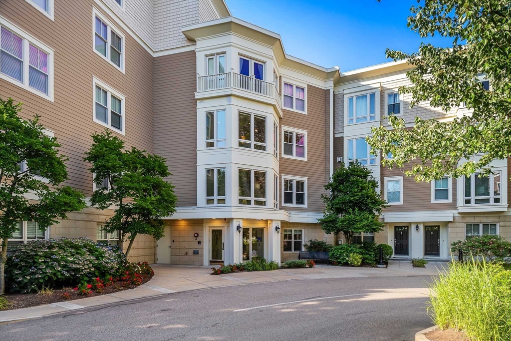 a front view of a multi story residential apartment building with yard and parking