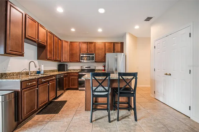 a kitchen with stainless steel appliances kitchen island granite countertop a table chairs sink and cabinets