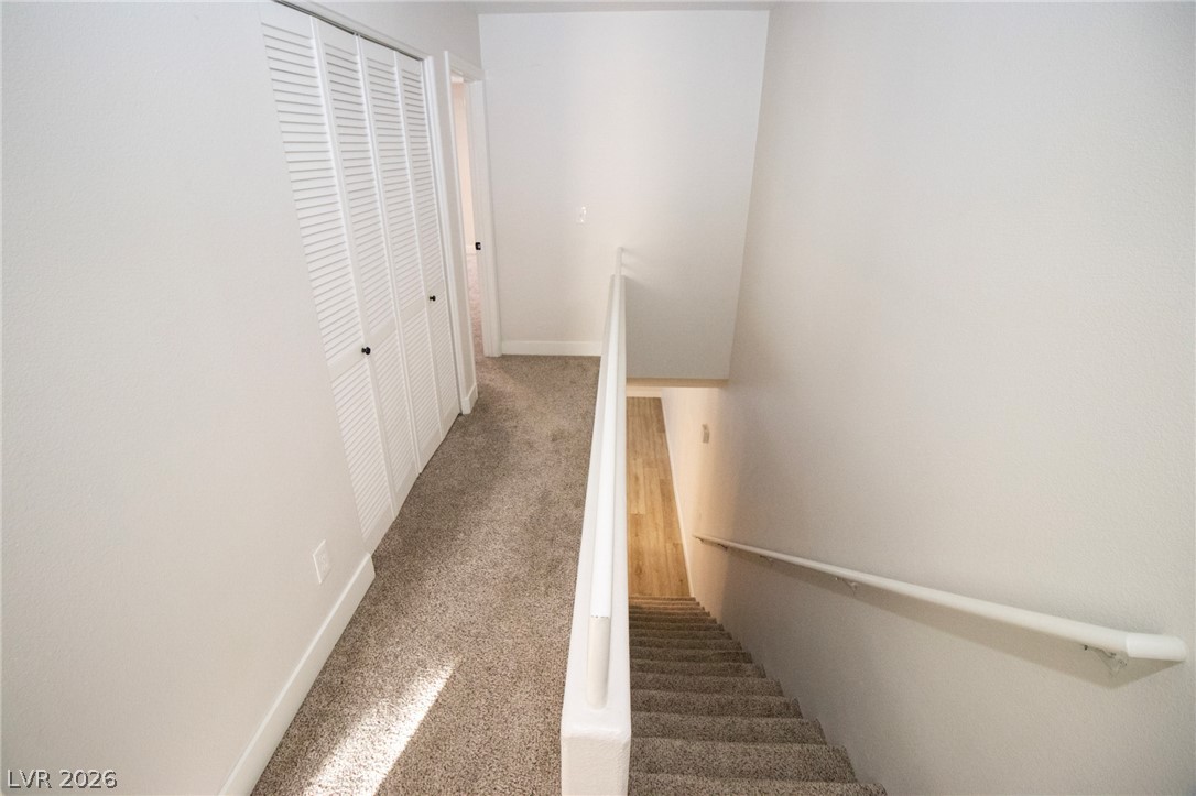 1468 Reef Ridge Court Las Vegas, NV 89128 - Photo 16 of 22 A split-level landing with carpeted stairs descends, complemented by louvered closet doors and a contrasting wood floor below.
