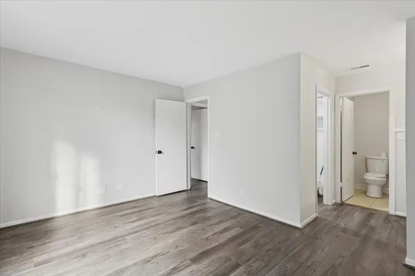a view of an empty room with wooden floor and a bathroom