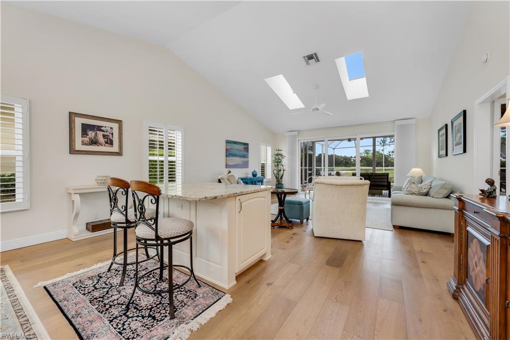 224 Edgemere Way South Naples, FL 34105 - Photo 8 of 35 Family room featuring a kitchen bar, light wood finished floors, high vaulted ceiling, light stone counters, and a skylight