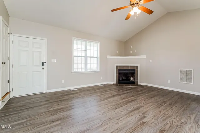 an empty room with wooden floor fireplace and windows