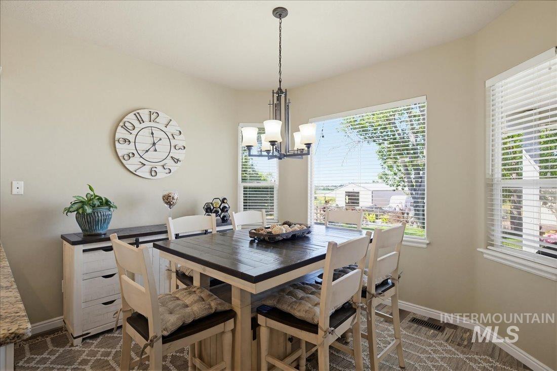 24623 Falcon Lane Caldwell, ID 83607 - Photo 10 of 40 Dining area featuring ample natural light, a contemporary chandelier, light-toned walls, wood-finish flooring, and white window blinds