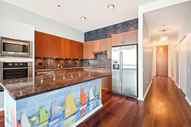 a kitchen with stainless steel appliances granite countertop a refrigerator a stove and a wooden floor