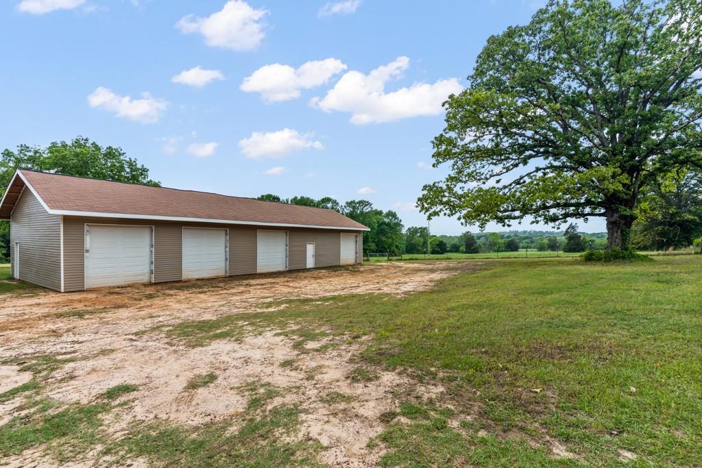 1129 Holly Road Gilmer, TX 75644 - Photo 3 of 31 Multi-bay outbuilding featuring a brown shingle roof, tan siding, and multiple white garage doors