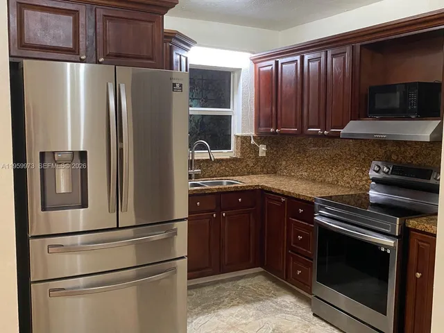 a view of a refrigerator in kitchen and an empty room
