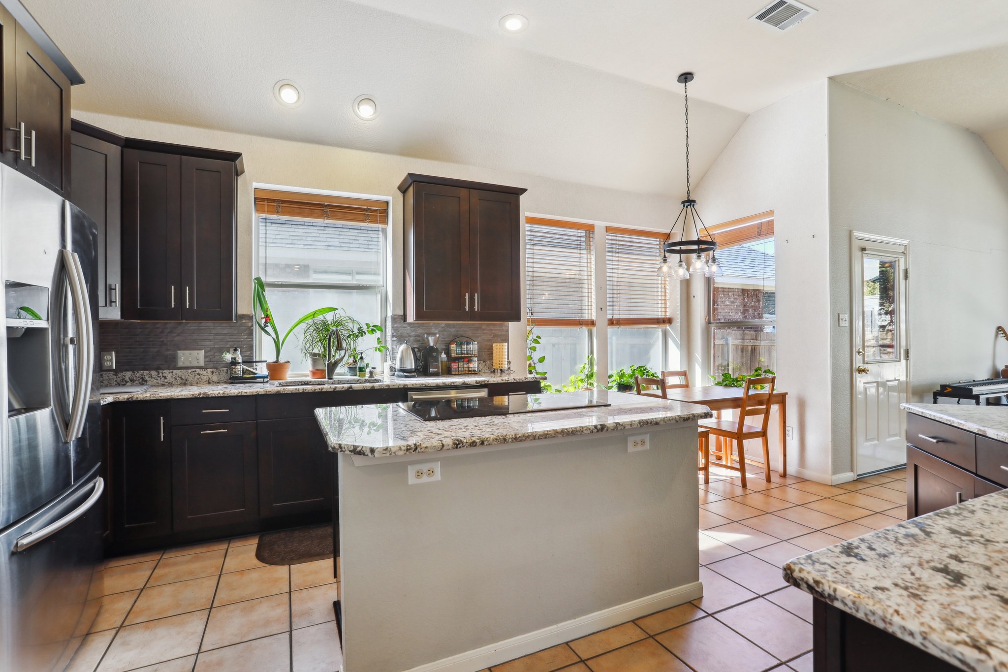 13541 Anarosa Loop Austin, TX 78727 - Photo 10 of 27 Open-concept kitchen featuring dark wood cabinetry, light granite countertops, stainless steel appliances, tile flooring, and recessed lighting