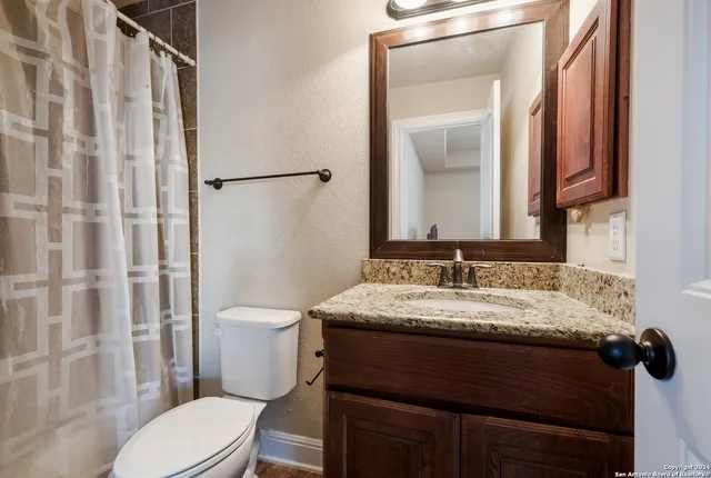 a bathroom with a granite countertop sink toilet a mirror and shower curtain