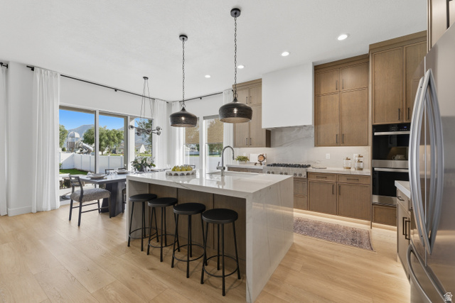 2559 West Aurora Avenue Mapleton, UT 84664 - Photo 6 of 60 Gourmet kitchen featuring a large central island with waterfall countertop, stainless steel appliances, a built-in double oven, and wood-finish cabinetry