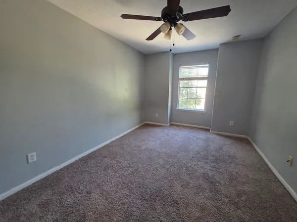 an empty room with a chandelier fan and windows