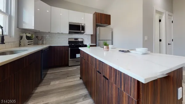 a kitchen with stainless steel appliances a sink dishwasher a stove top oven a refrigerator with grey cabinets and wooden floor