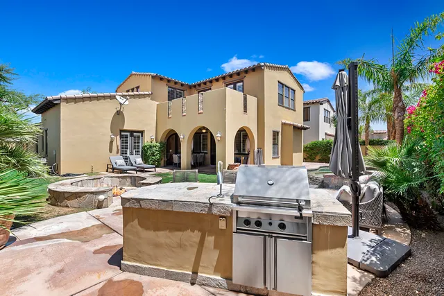 a view of a white house with large windows and a table and chairs under an umbrella