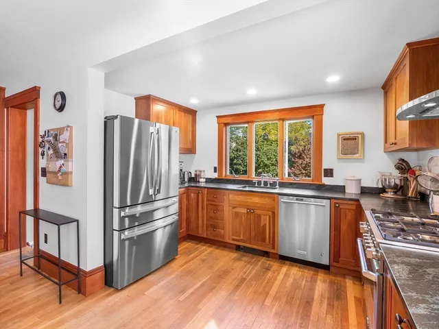 a kitchen with stainless steel appliances granite countertop a stove a refrigerator a sink a dining table and chairs with wooden floor