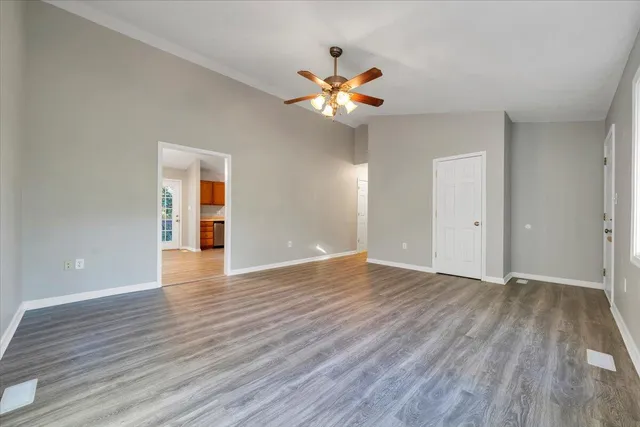 a view of an empty room with wooden floor and a ceiling fan