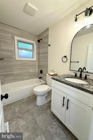 a bathroom with a granite countertop sink a toilet a mirror and bathtub