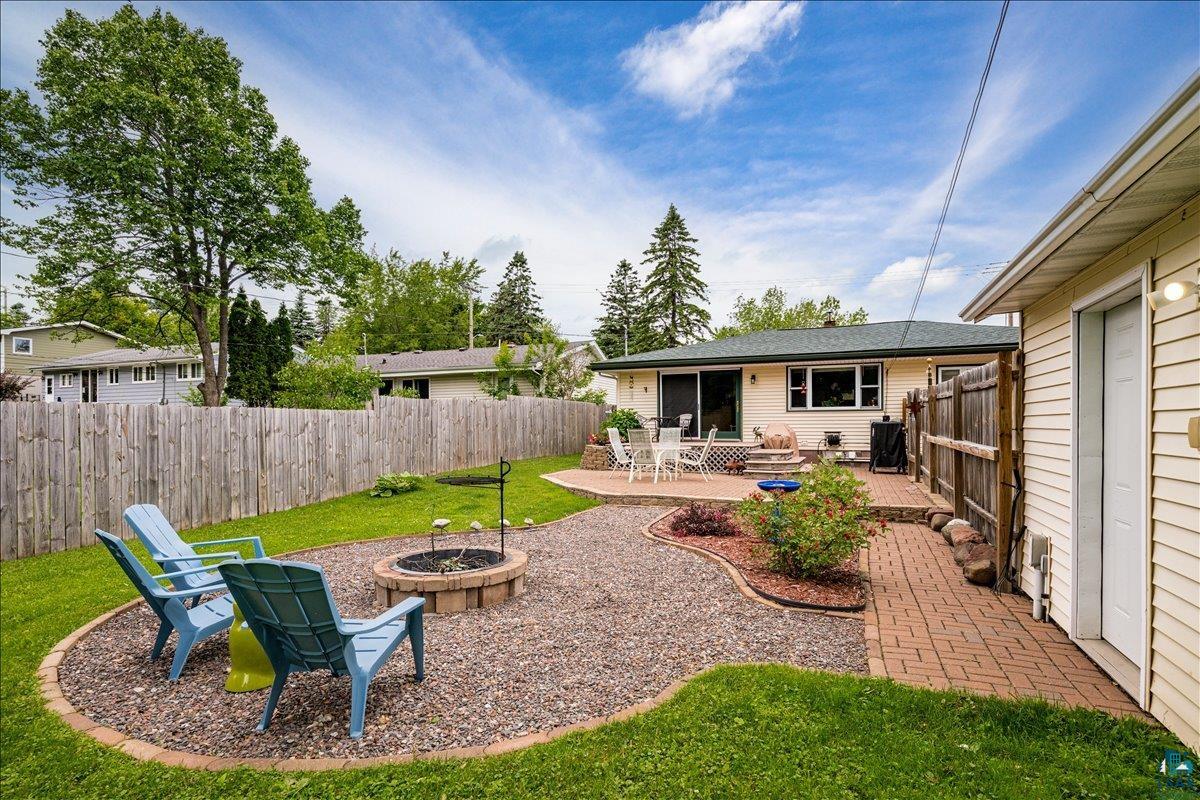 130 West Austin Street Duluth, MN 55803 - Photo 24 of 35 Private backyard featuring a fenced perimeter, a fire pit area with gravel ground cover, a brick paver pathway, a stone patio, and established landscaping
