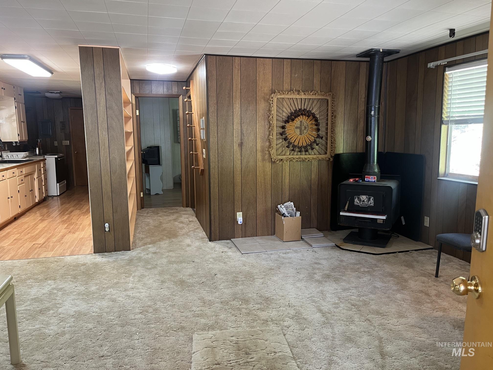 39 Mayflower Mine Road Placerville, ID 83666 - Photo 15 of 36 Living space featuring wood paneling, a dark-toned wood-burning stove on a hearth, and carpeting
