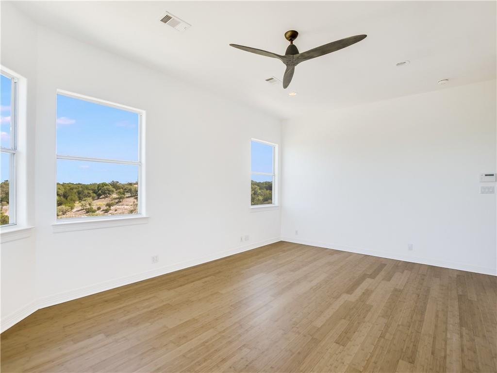 13301 Lone Rider Trail Bee Cave, TX 78738 - Photo 11 of 21 Spacious room featuring light-toned wood flooring, clean white walls, a ceiling fan, and multiple windows offering views of the natural landscape